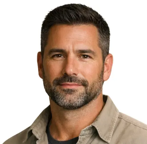 Headshot of bearded man with short dark hair wearing beige shirt on gray background.